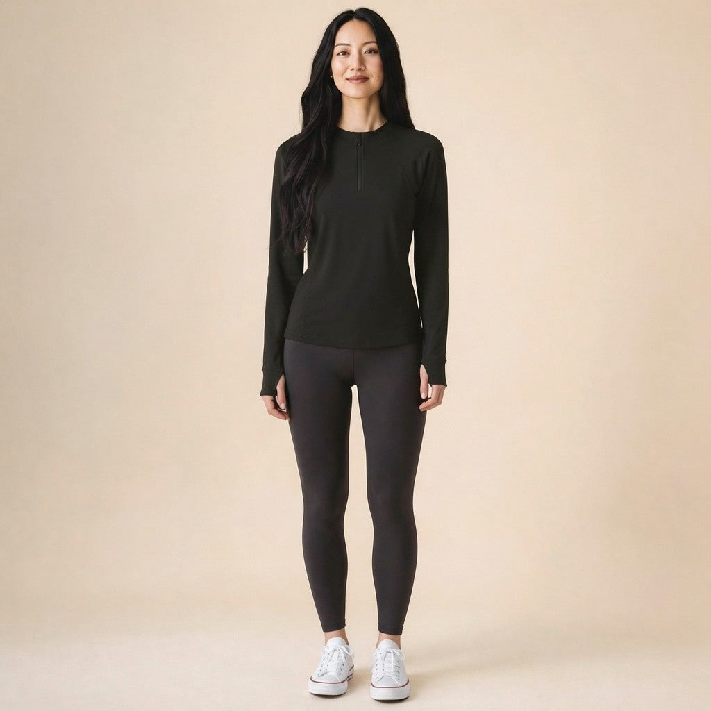 Woman wearing a black quarter-zip long-sleeve running top with thumbhole cuffs, front view